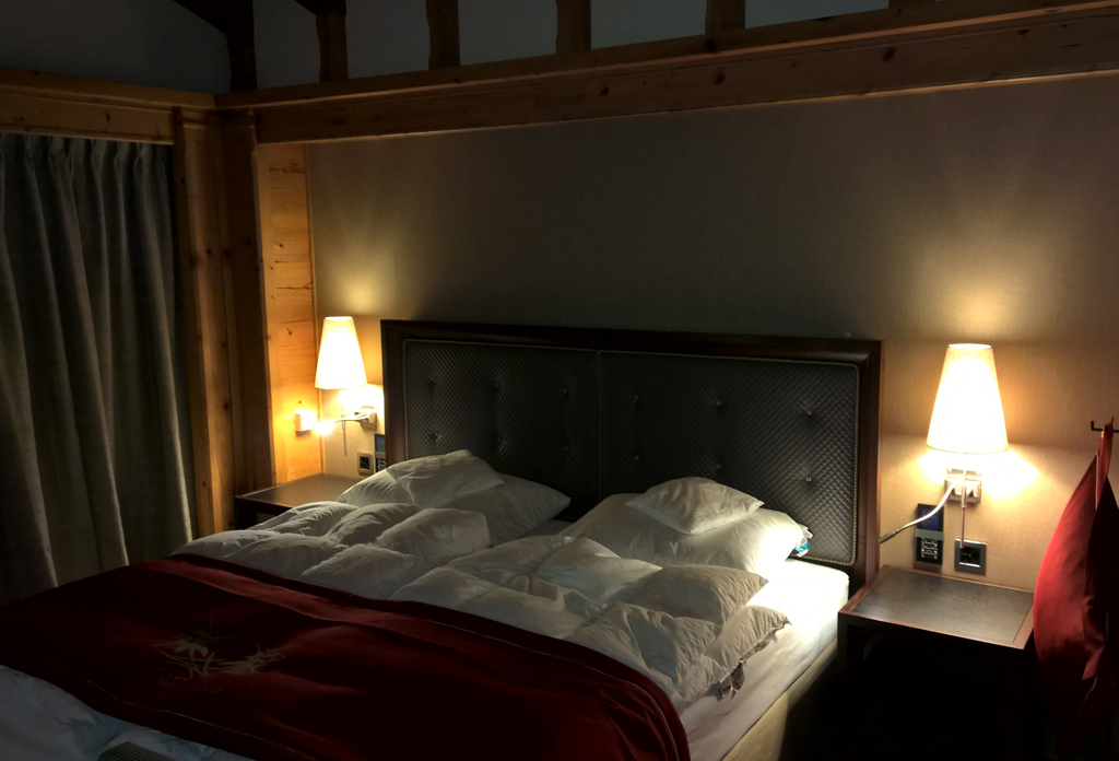 Ein Schlafzimmer mit Wandleuchten auf jeder Seite eines wunderschön gemachten Bettes mit zwei Bettdecken und Beistelltischen.